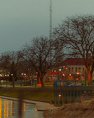 Elkhart Riverwalk along the St Joseph River at dusk with park lights, pedestrian bridge, and historic downtown buildings in Elkhart Indiana.