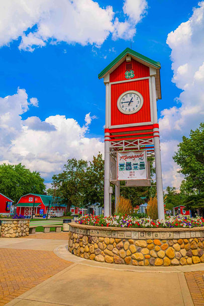A wide shot of the Clocktower in the center of Heritage Park with a blue sky and flowers planted around the clock tower
