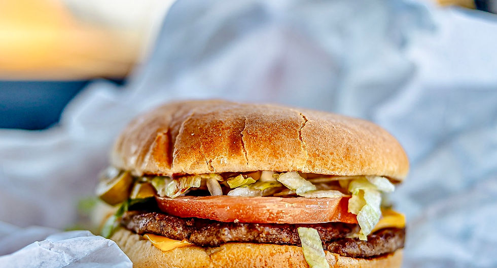 Olive cheeseburger sitting on crumpled white paper inside a car