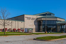Exterior of the Northern Indiana Event Center at the RV Hall of Fame in Elkhart Indiana, showing the main glass entrance and parking area on a clear blue sky day.