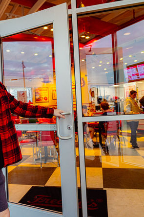 Customer opening glass door into Freddy’s Frozen Custard & Steakburgers dining area in Elkhart, Indiana