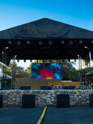 Escenario profesional para conciertos al aire libre con torres de truss de aluminio, techo de lona negra, pantalla LED central y sistemas de sonido en la base.