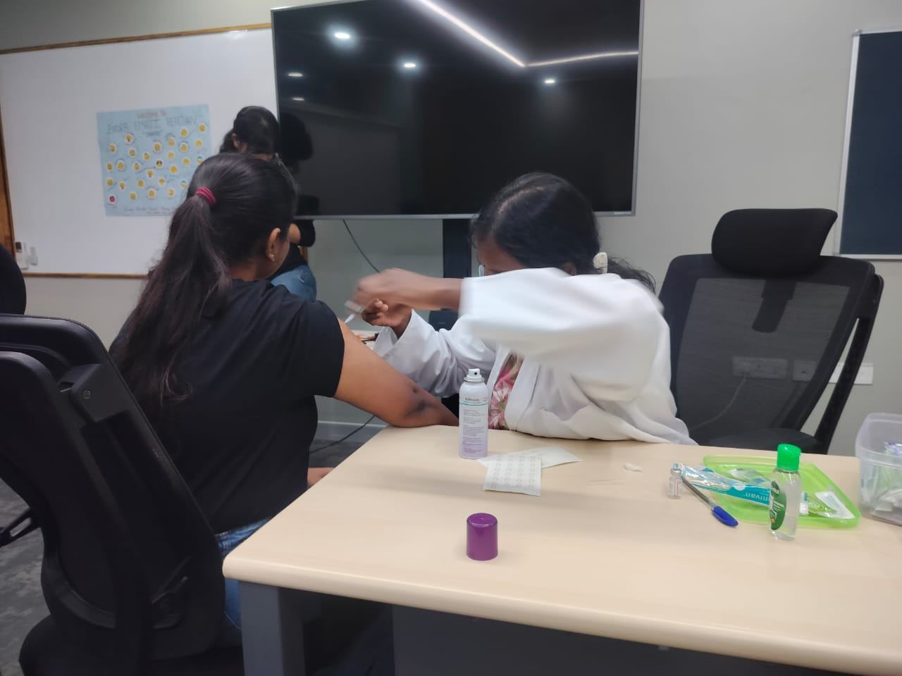 A Vaccine Hub Clinic nurse giving a vaccine to an employee in an office meeting room
