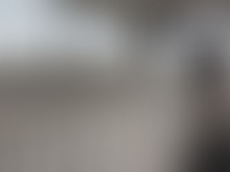 Person wearing a black The Riviera Group hoodie cleaning a glass door in a hallway with white railings. Overcast sky visible through windows.