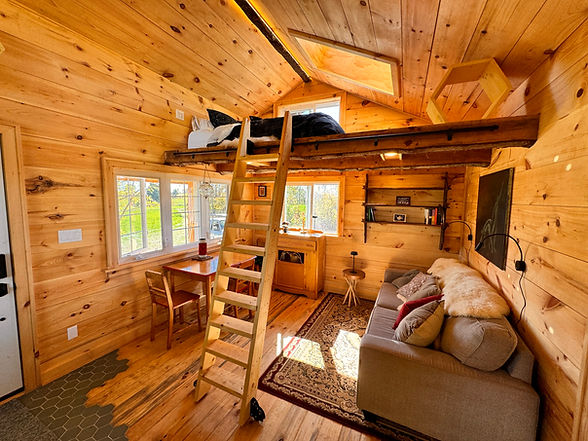 Welcome to the heart of our rustic cabin at Glen Colton Farm. With its charming shiplap pine walls and a stunning timber-framed loft featuring a skylight, this space is a perfect blend comfort and nature. The handmade wooden ship ladder on bookshelf sliders adds a unique touch, the living room, bathed in natural light from numerous windows, invites warmth and relaxation. Experience the perfect that combines rustic charm with modern living.