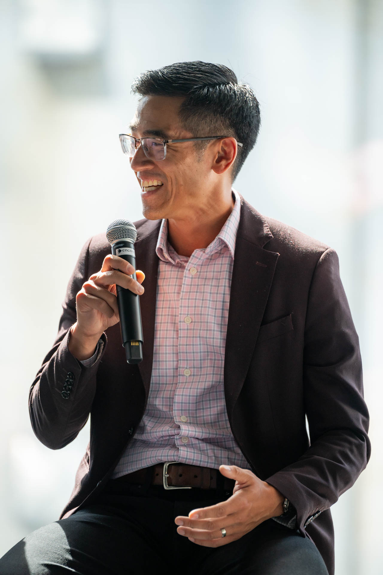 Man smiling and speaking into a microphone at an event.