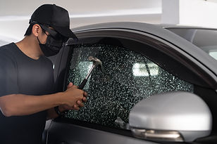Thief with mask breaking car window with hammer on day time. Car thief, car theft concept.