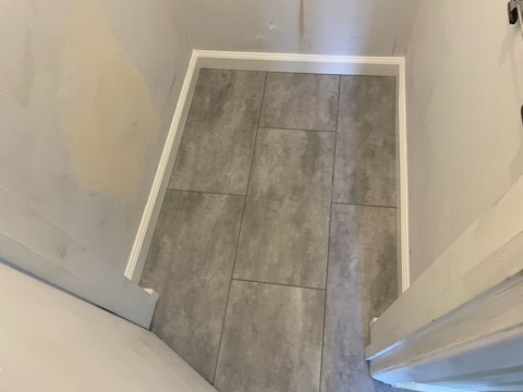 Close-up of precision-cut vinyl tiles being expertly fitted in a restroom. The grey tiles add a contemporary touch, perfectly aligned for a flawless appearance.