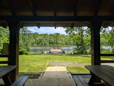 a view of a dock on a river from the inside of a picnic pavilion