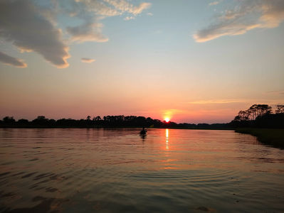 a kayaker paddles into the sunset on calm water and trees in the background