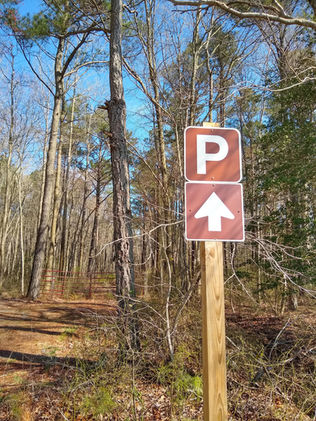 A sign in the woods pointing to a parking area