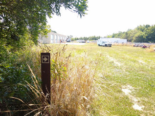 A trail marker on the edge of the woods next to a yard with some trucks