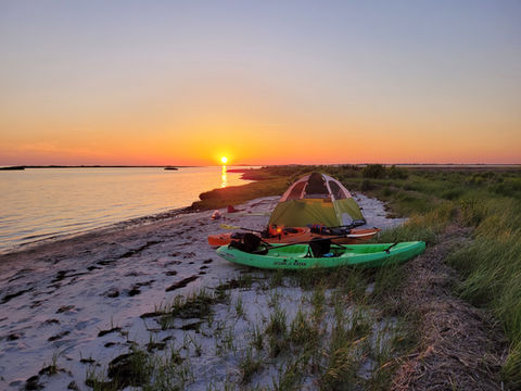 two kayaks and a tent on a beach at sunset