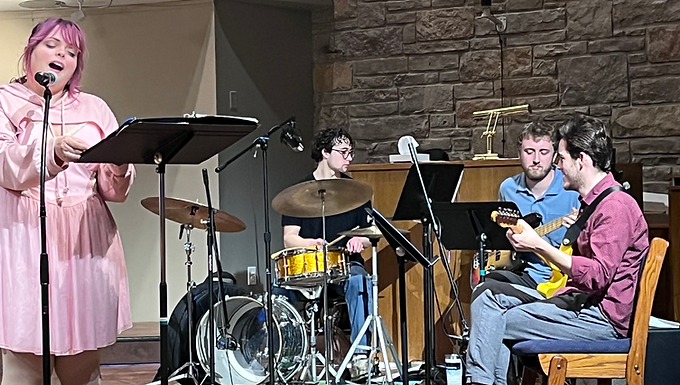A vocalist, a drummer, a guitarist and a bass player play on an elevated chancel.