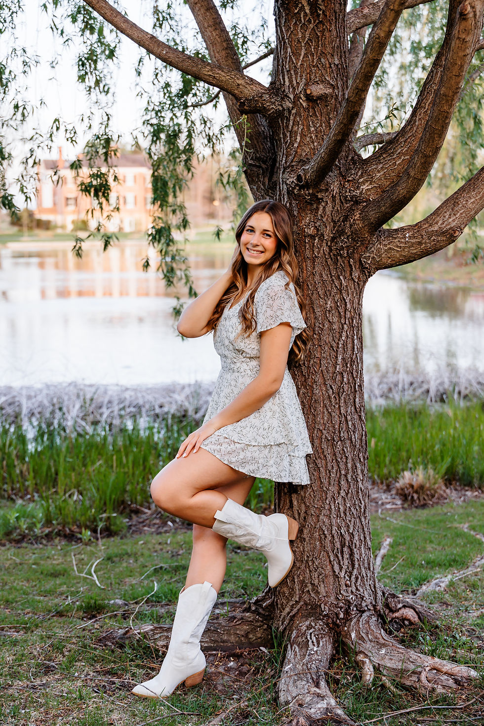 A woman in a floral dress and white boots leans against a tree, smiling.best senior portrait photographers, family photographer, Geneva IL senior portraits, Wheaton senior portraits, west suburbs senior portrait photographers