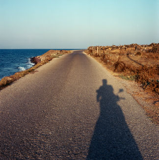 Shadow of a person on a motorcycle on a coastal road.