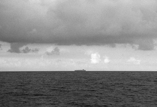 Black and white horizon view of a ship under cloudy skies