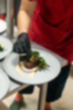 A gloved hand places a garnish on a meal.