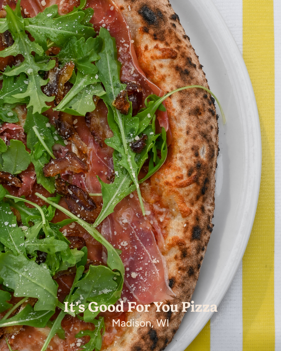 A pizza with arugula from It's Good For You Pizza on a white plate.