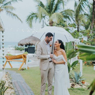 Bride and groom under white umbrella in tropical setting.