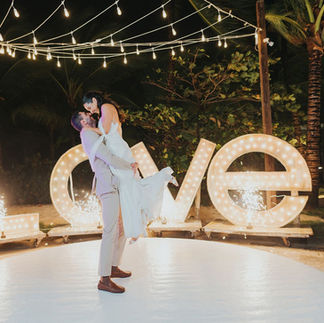 Groom lifting bride during first dance with fireworks in front of Love sign at Kukua.