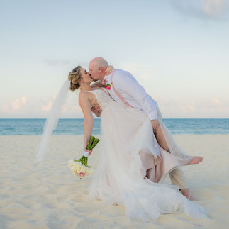 Groom dipping bride on the sand with an ocean backdrop.