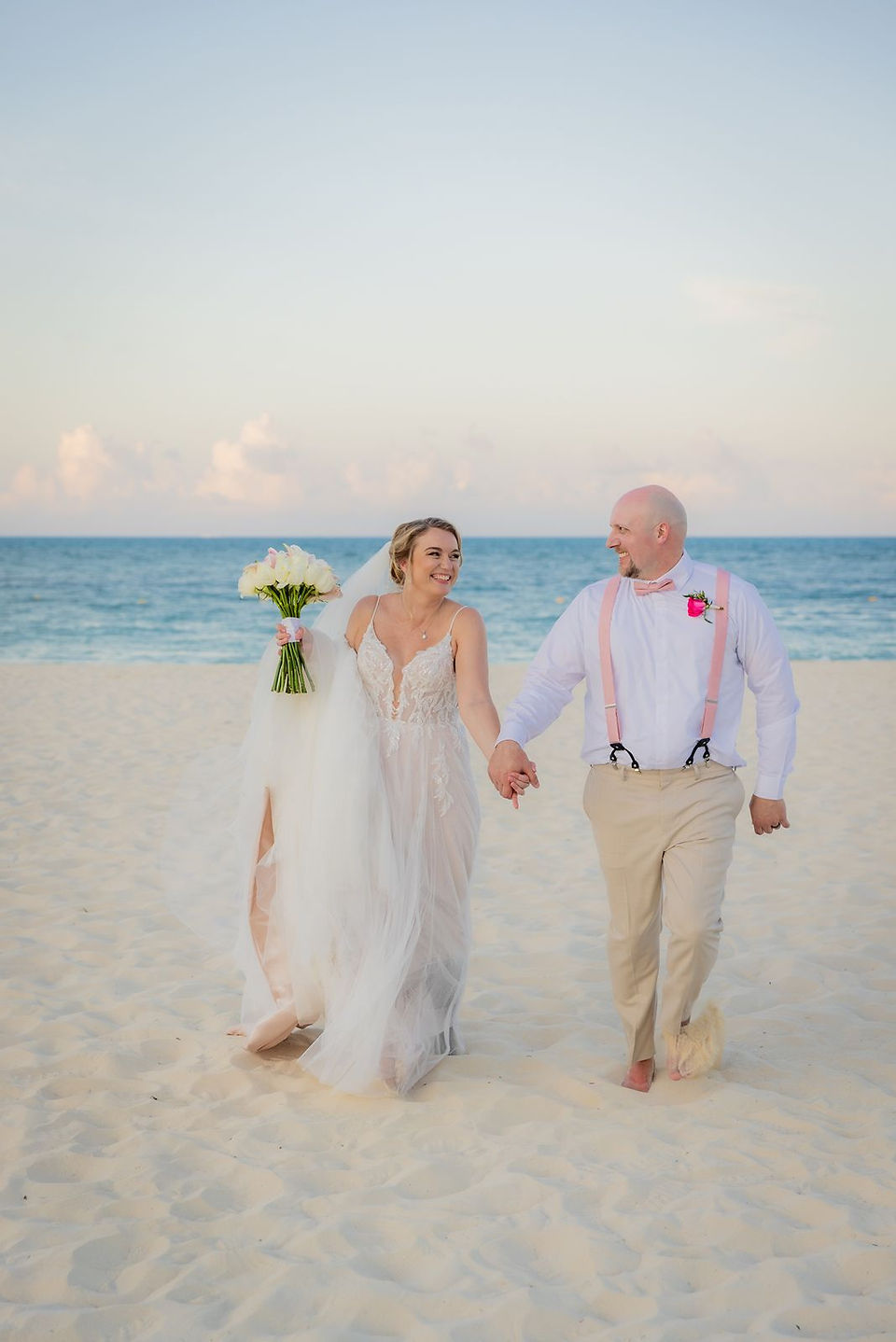 Bride and groom walking on the beach together.