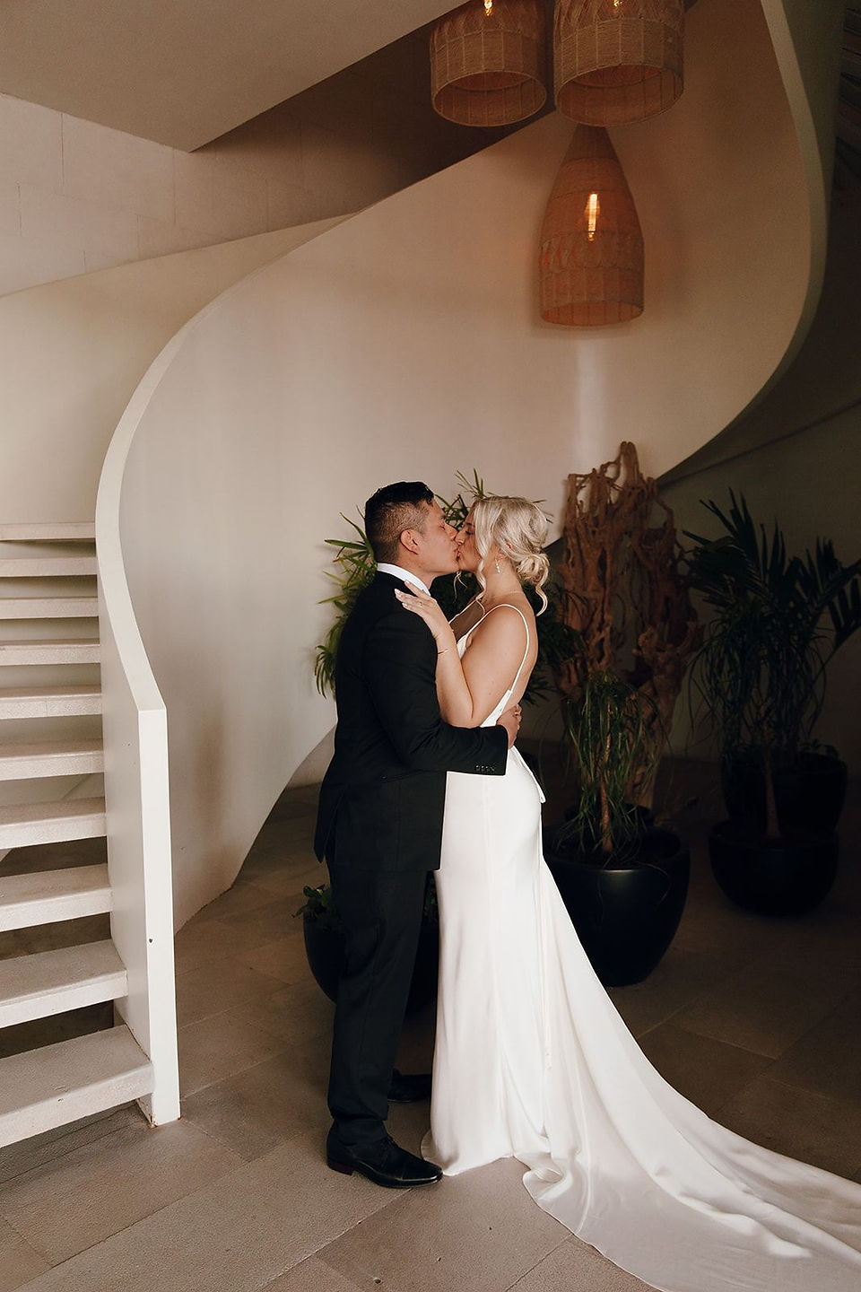 Bride and groom in tuxedo kissing by spiral staircase at Dreams Vista Cancun.