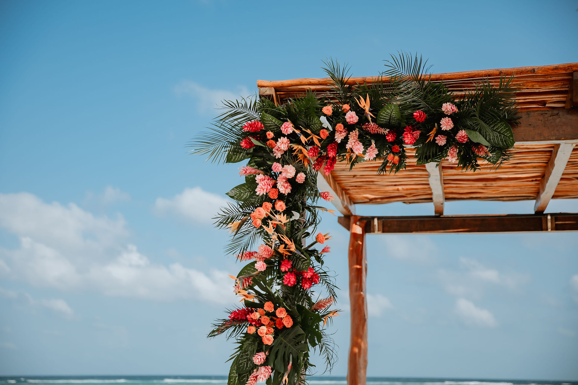 Tropical floral decor on ceremony arch at all inclusive wedding at Secrets Akumal in Mexico planned by travel agent for destination weddings, EverAfter Travel.