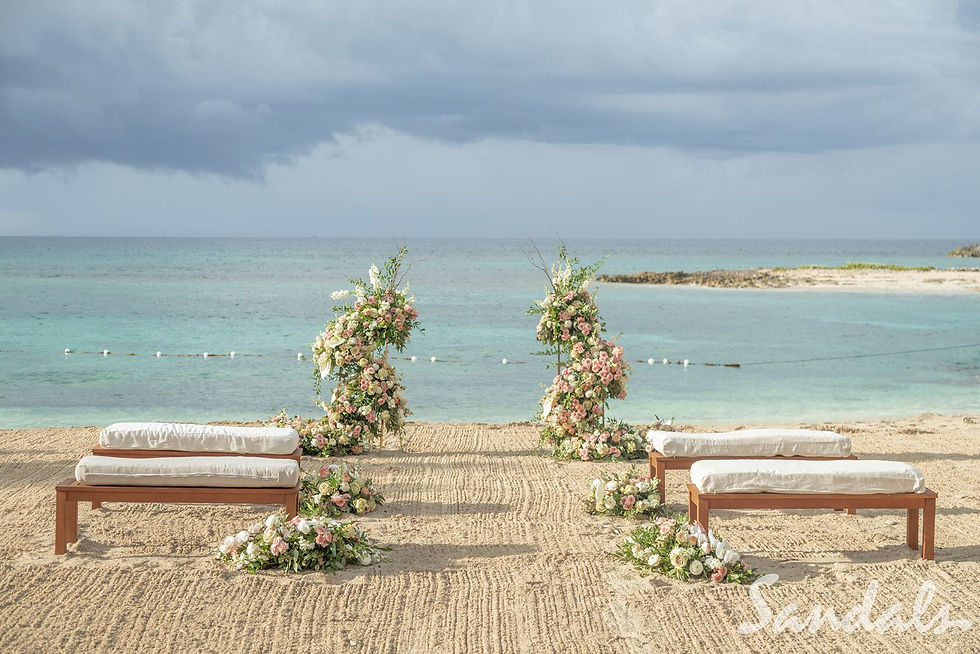 Beach wedding setup with floral arches and benches on sand with calm turquoise water in the background at a Sandals resort in the Caribbean.