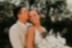 Groom kissing bride's cheek in lush greenery with a white bouquet at their Dreams Sapphire wedding in Mexico.