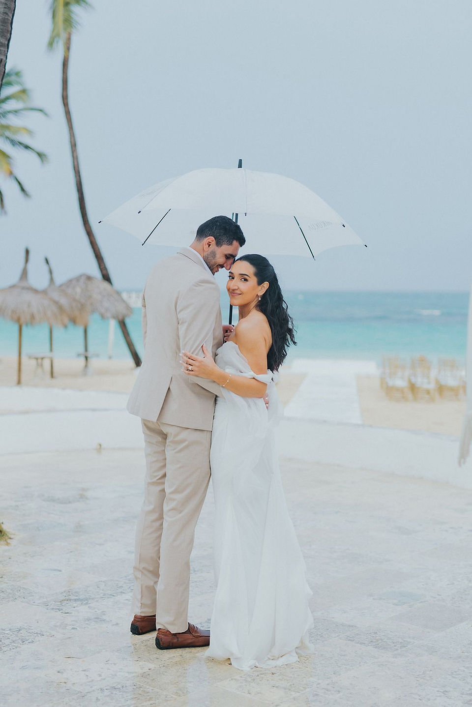 Bride and groom under a white umbrella in front of the ocean.