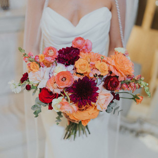 Bride holding colorful bridal bouquet with coral and red flowers.
