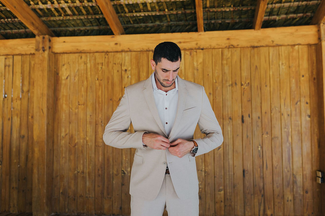 Groom putting on beige suit.