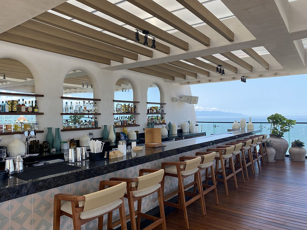 Unico Riviera Nayarit Alto rooftop bar with empty wooden chairs, a stocked liquor shelf, and a sea view.