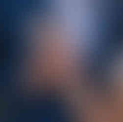 Close-up of bride and groom holding hands, highlighting their wedding rings against the groom’s navy suit and white shirt, with a white rose boutonniere.