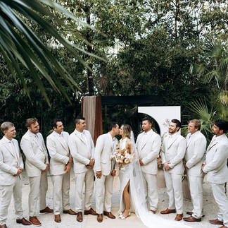 Bride and groom kissing in front of groomsmen in beige suits at jungle wedding in Tulum, Mexico.