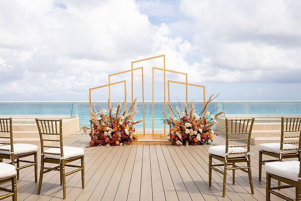 Oceanfront setting with chairs facing a geometric wooden frame adorned with vibrant flowers.