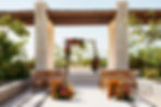 Courtyard Plaza wedding venue at Secrets Playa Blanca resort with wooden chairs, a floral arch of colorful tropical flowers, stone pillars, and lush greenery.