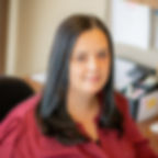 Jenny Tzortzos in a maroon shirt sitting at a desk