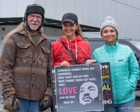 A man and two women, dressed in jackets and hats, stand around a sign featuring a black-and-white image of Martin Luther King, Jr.s face