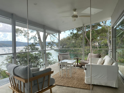 Serene outdoor entertaining area overlooking Pittwater Estuary, styled with inviting furnishings for Airbnb guests.