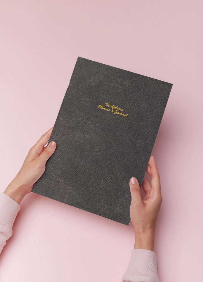 Hands holding a journal, with text reading, Mindful Journals, on pink background.