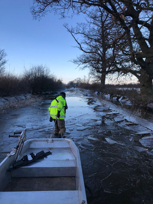 Person in bright jacket in frozen canal with boat