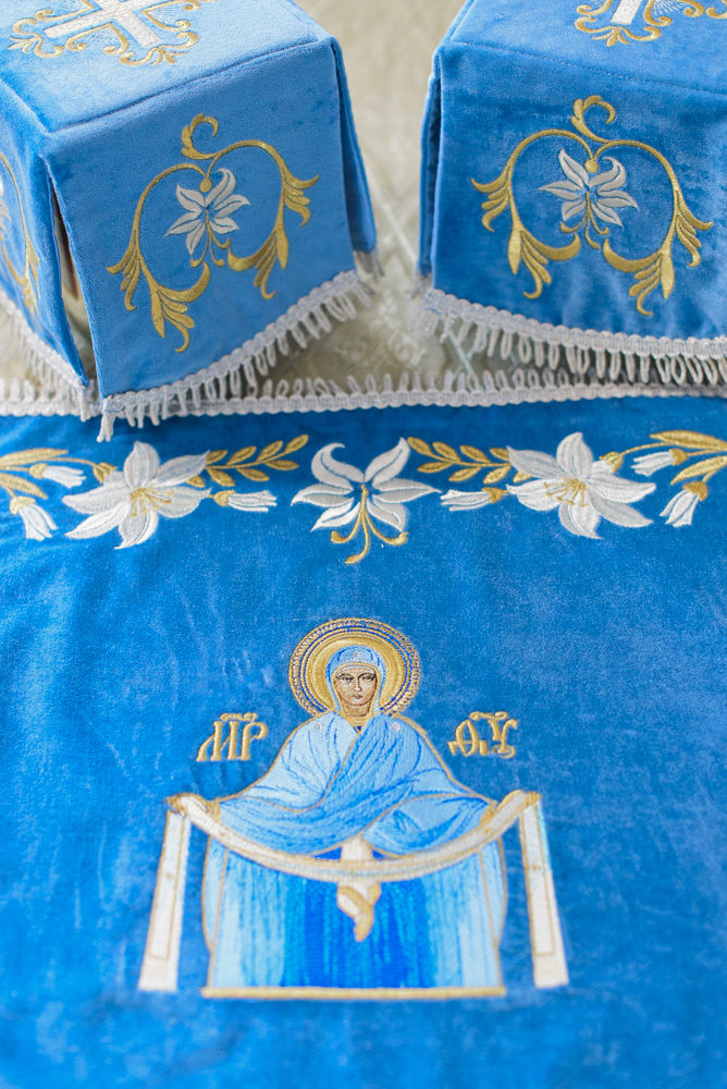 Close-up of embroidered lilies and Virgin Mary icon on blue velvet Orthodox altar cover.