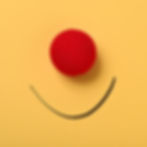 A clown red nose and a hand-drawn smile over a yellow paper background