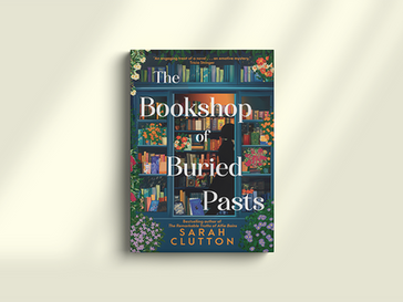 Book cover of "The Bookshop of Buried Pasts" by Sarah Clutton, featuring colorful bookshelves adorned with flowers against a light beige backdrop.