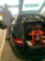 Black Porsche 911 receiving a jumpstart service at Hartsfield-Jackson Airport for a dead battery emergency.