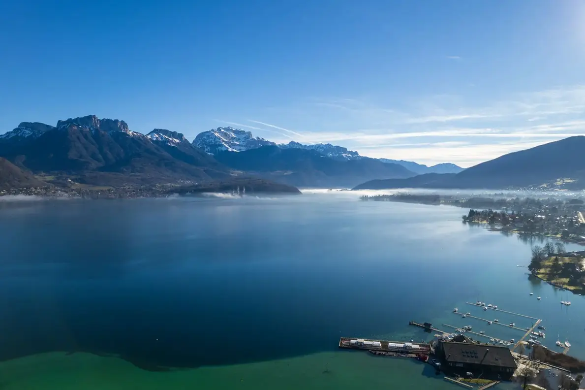 Vue aérienne du lac d’Annecy aux eaux turquoise, du port de Sevrier et des montagnes en arrière-plan, Haute-Savoie