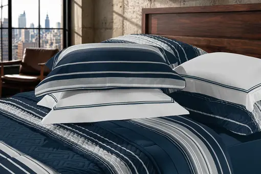 Detalhe de jogo de cama fotografado em ambiente decorado para catálogo, e-commerce e campanhas publicitárias da indústria têxtil.